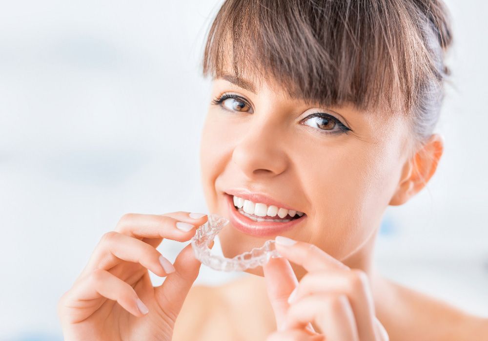 A woman is smiling while holding a clear brace in her mouth.