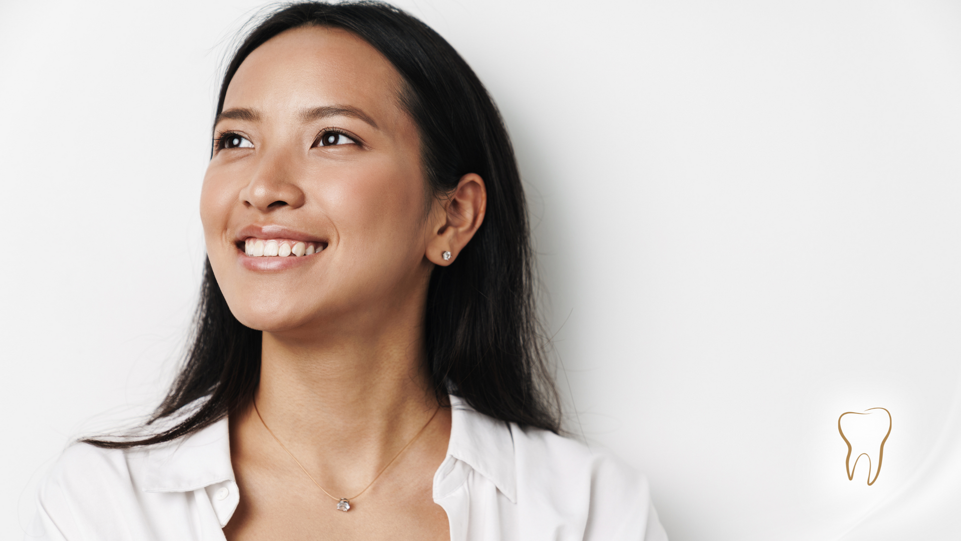 A woman is smiling and looking up against a white wall.