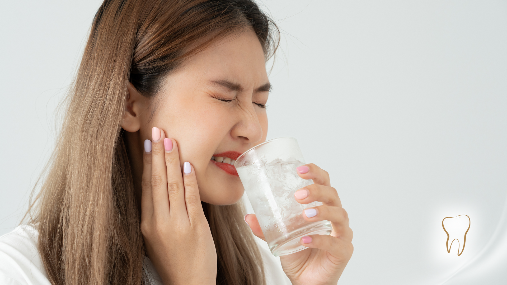Woman with toothache holding a glass of water, wincing in pain, against a white background.