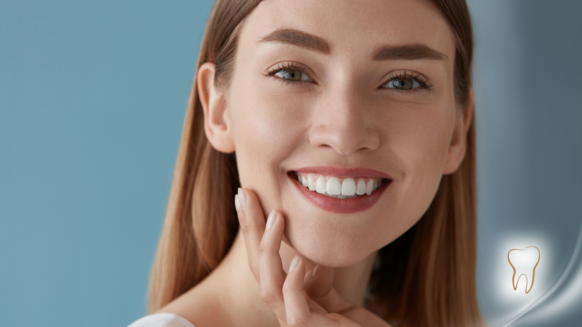 Woman smiling, touching her cheek. She has perfect, white teeth against a blue backdrop.