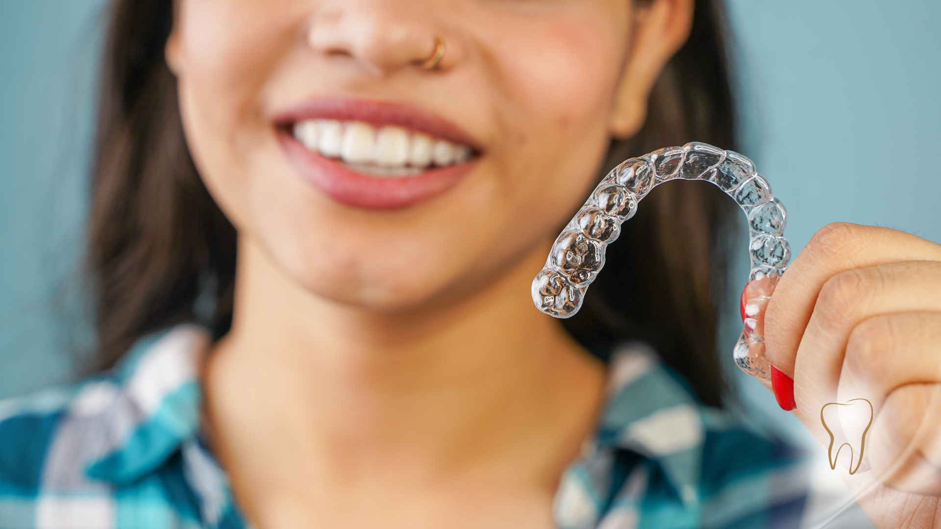 A woman is holding a clear retainer in front of her teeth.