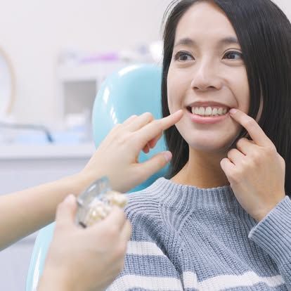 A woman is sitting in a dental chair while a dentist examines her teeth.