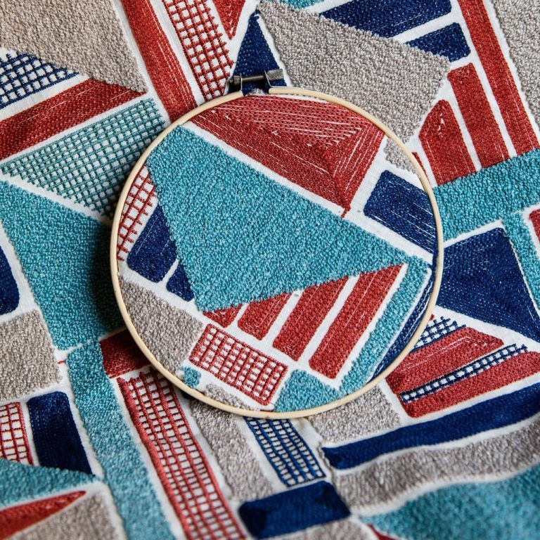 A embroidery hoop is sitting on top of a colorful fabric.
