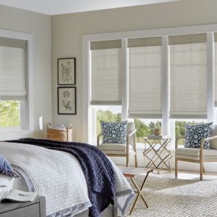 A bedroom with a bed , chairs , and roman shades on the windows.