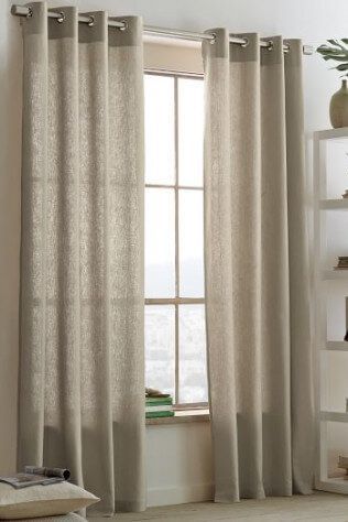 A pair of beige curtains are hanging on a window in a living room.