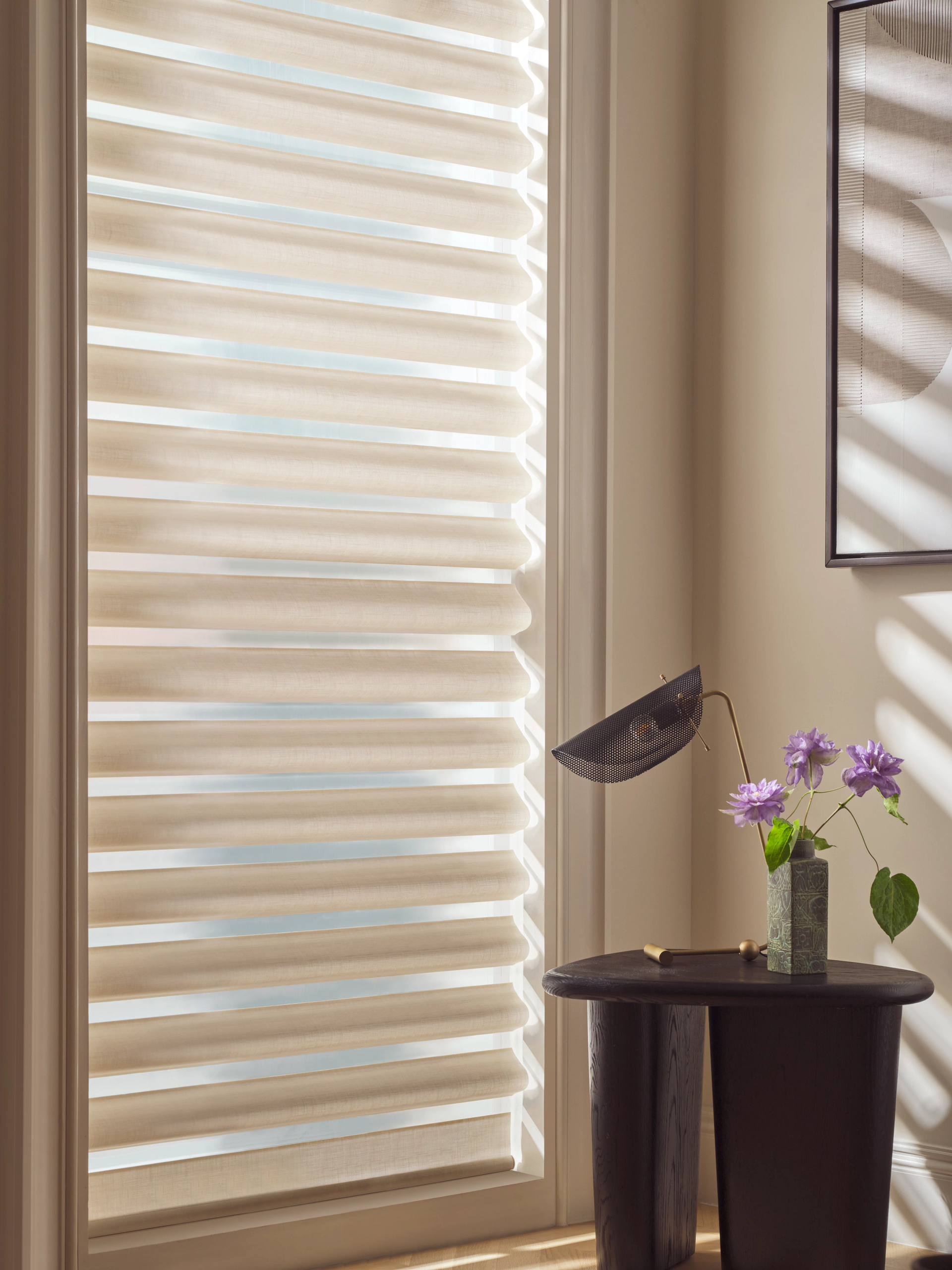 There is a table with flowers on it in front of a window with blinds.