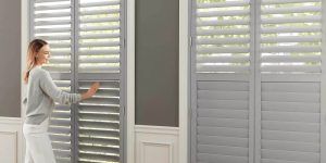A woman is standing in front of a window with shutters on it.