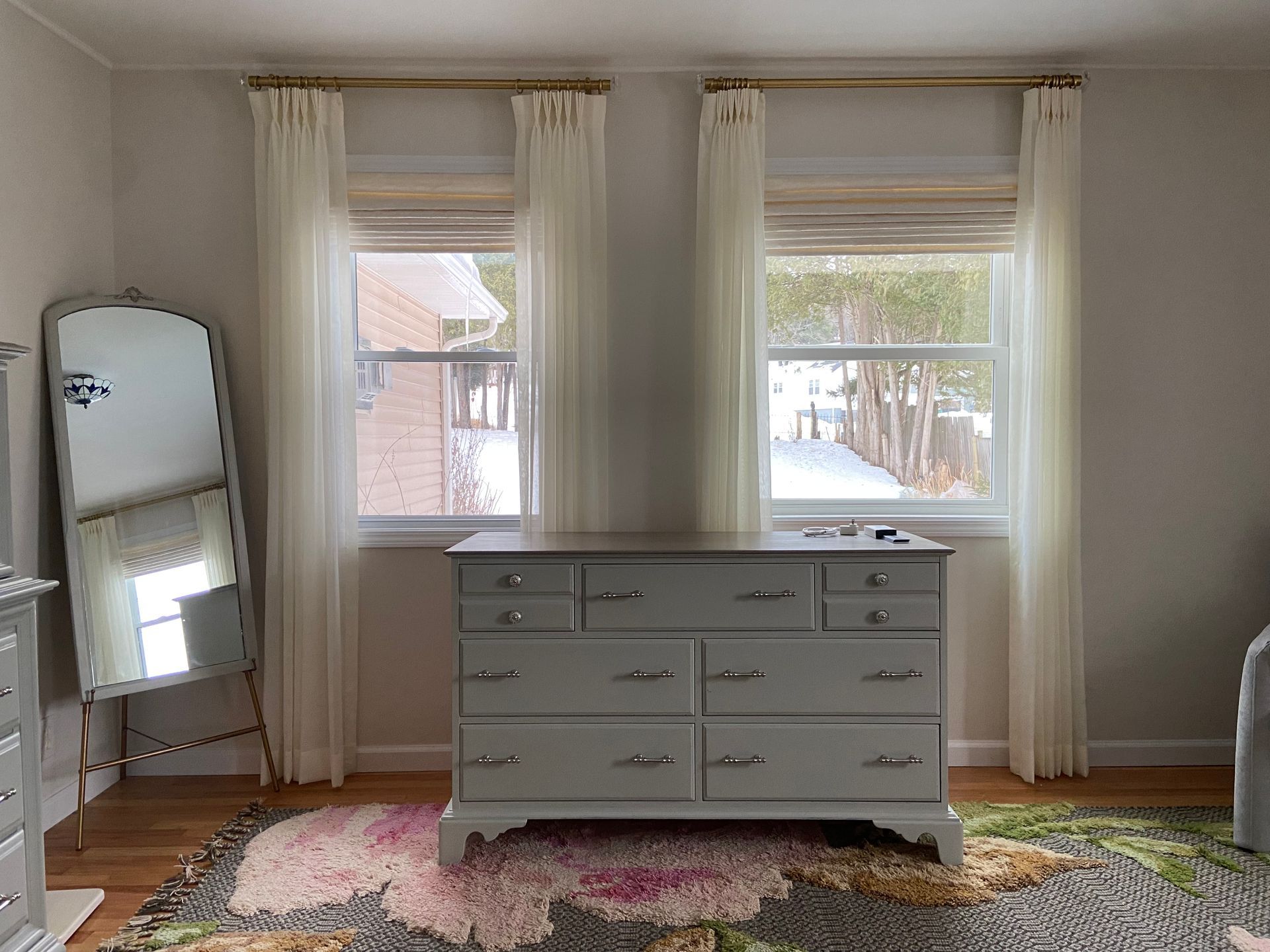 A bedroom with a dresser , mirror , rug and two windows.