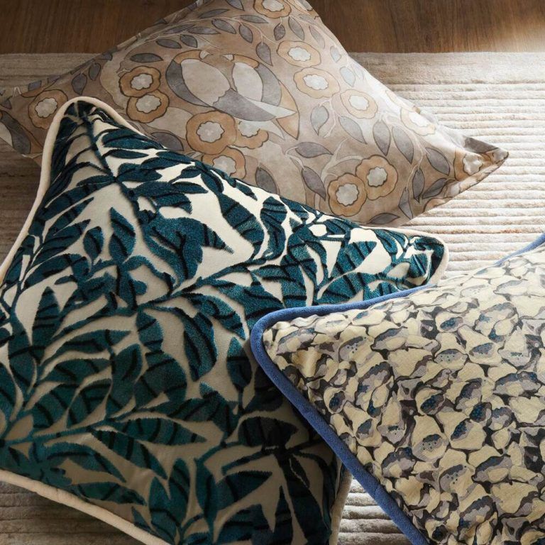Three pillows are sitting on a rug including one with leaves on it