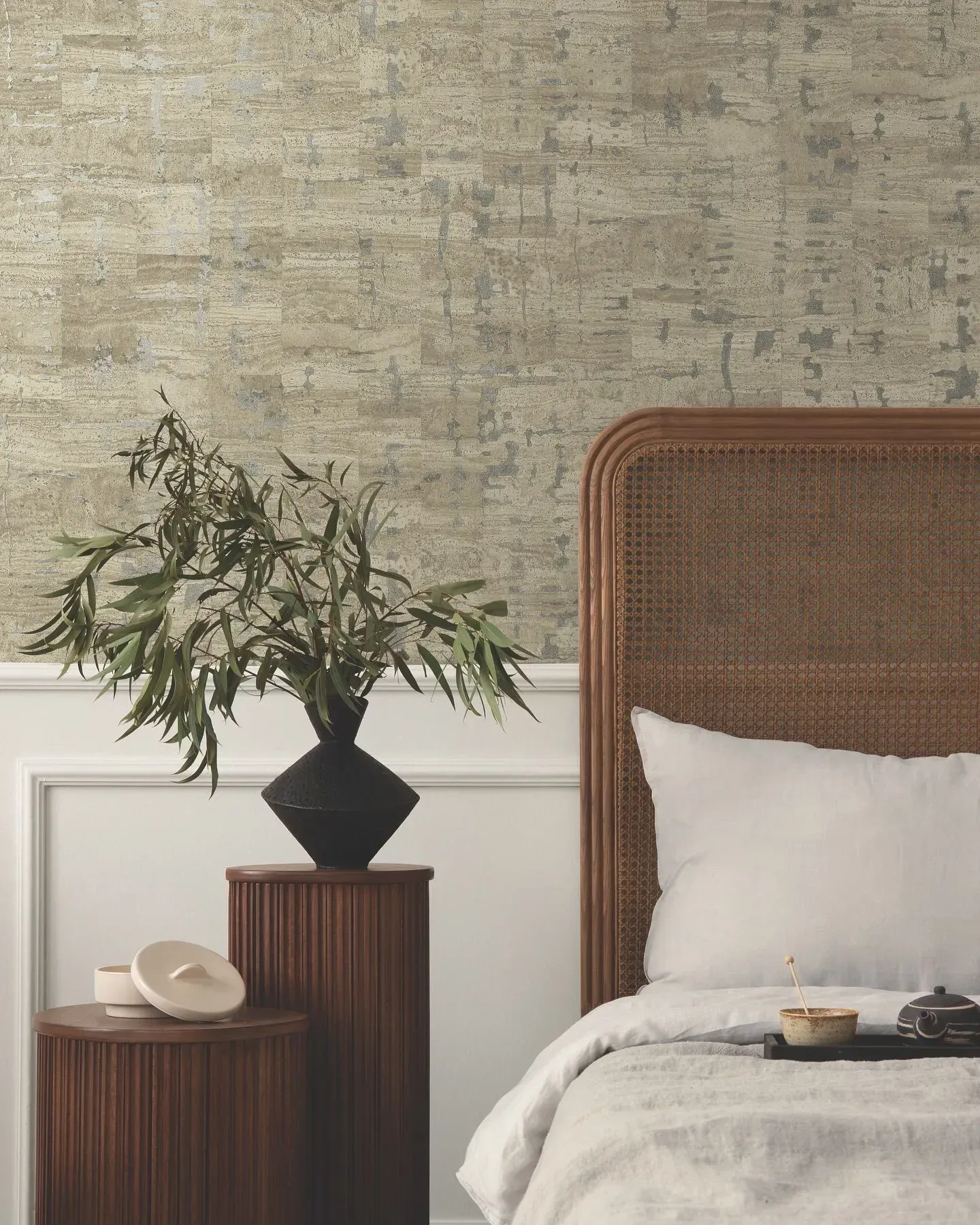 A bedroom with a wicker headboard and a plant on a nightstand.