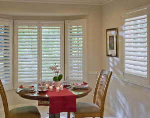 A dining room with a table and chairs and shutters on the windows