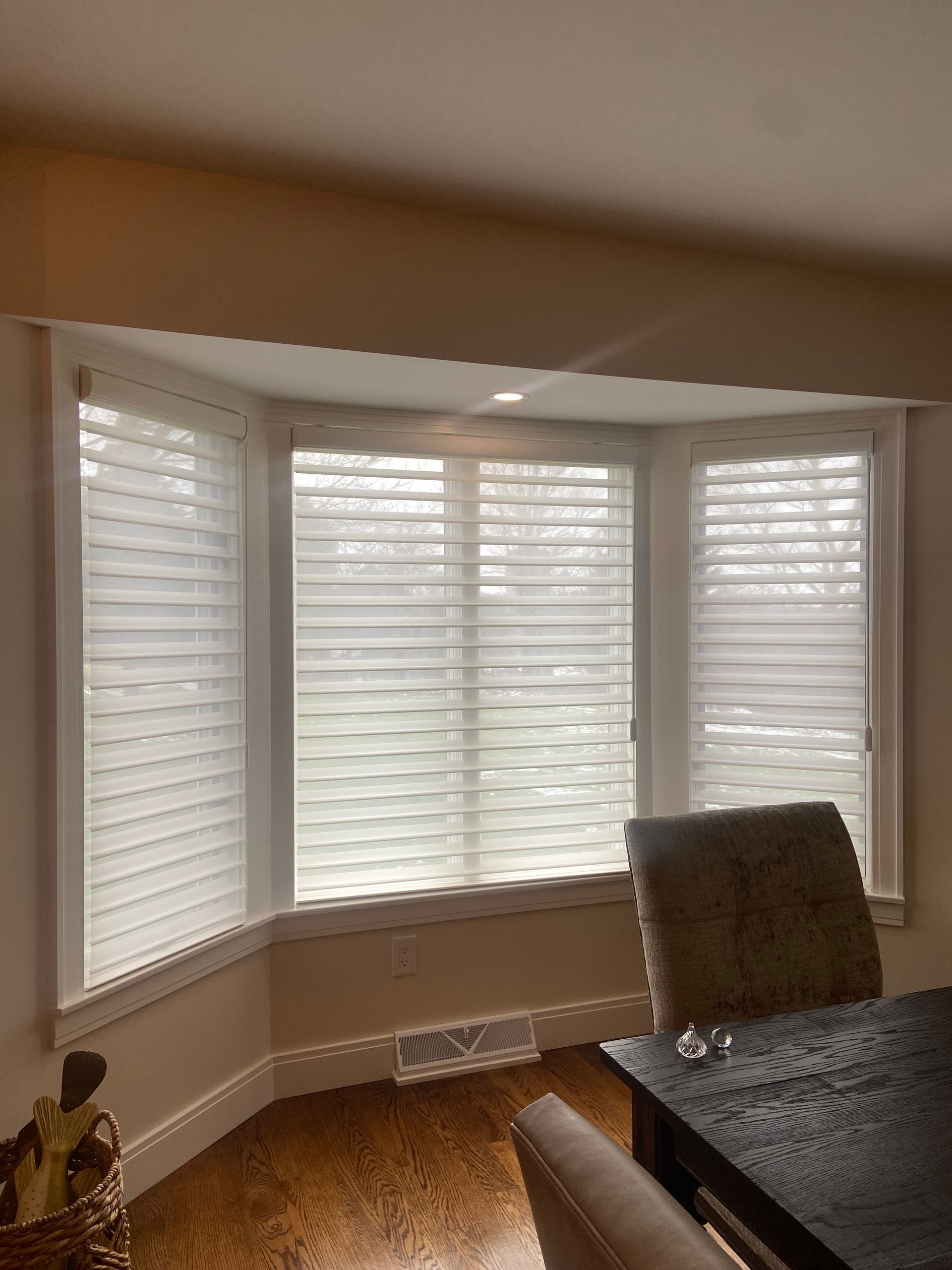 A dining room with a table and chairs and a bay window with white blinds.