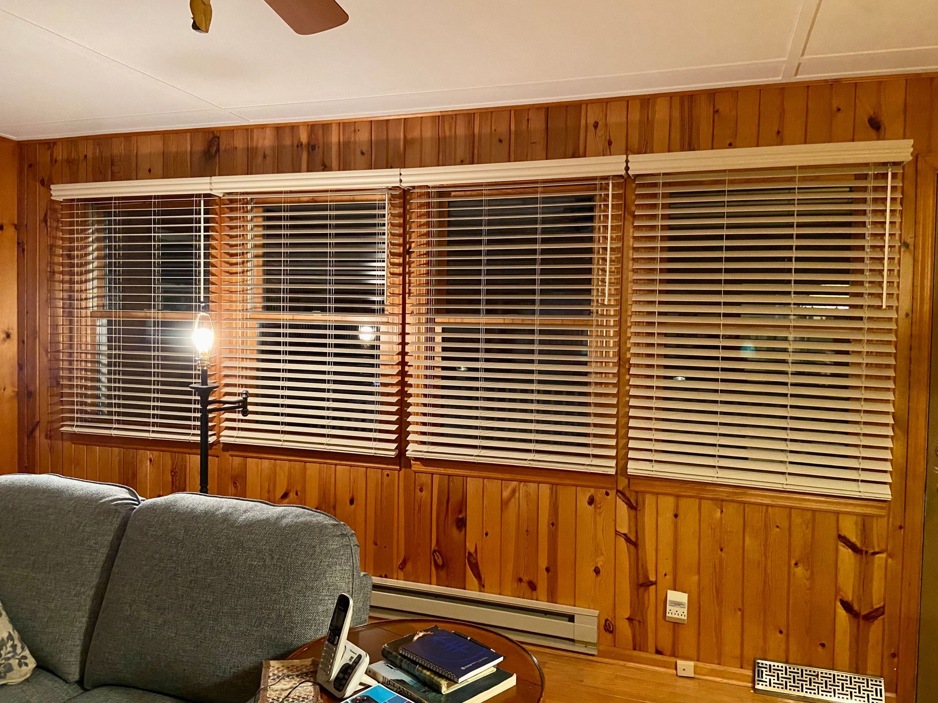 A living room with wood paneling and blinds on the windows