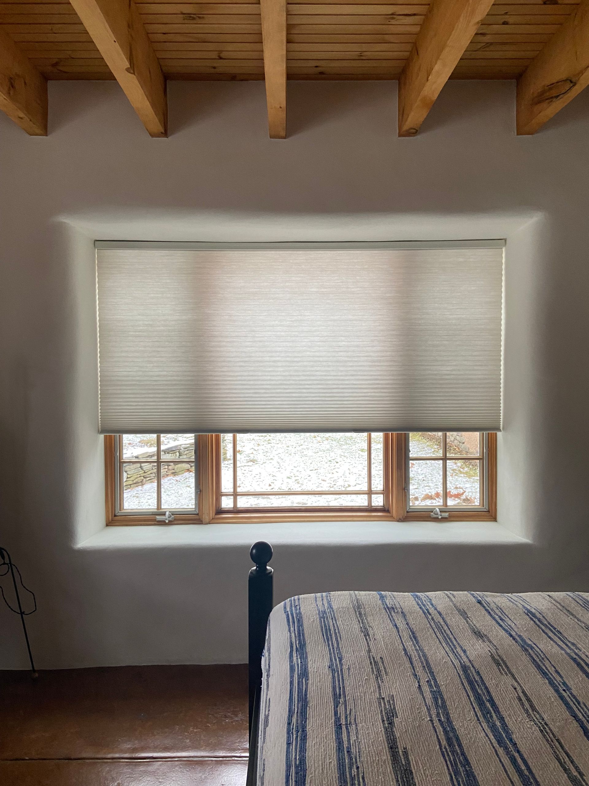 A bedroom with a bed and a window with blinds on it.