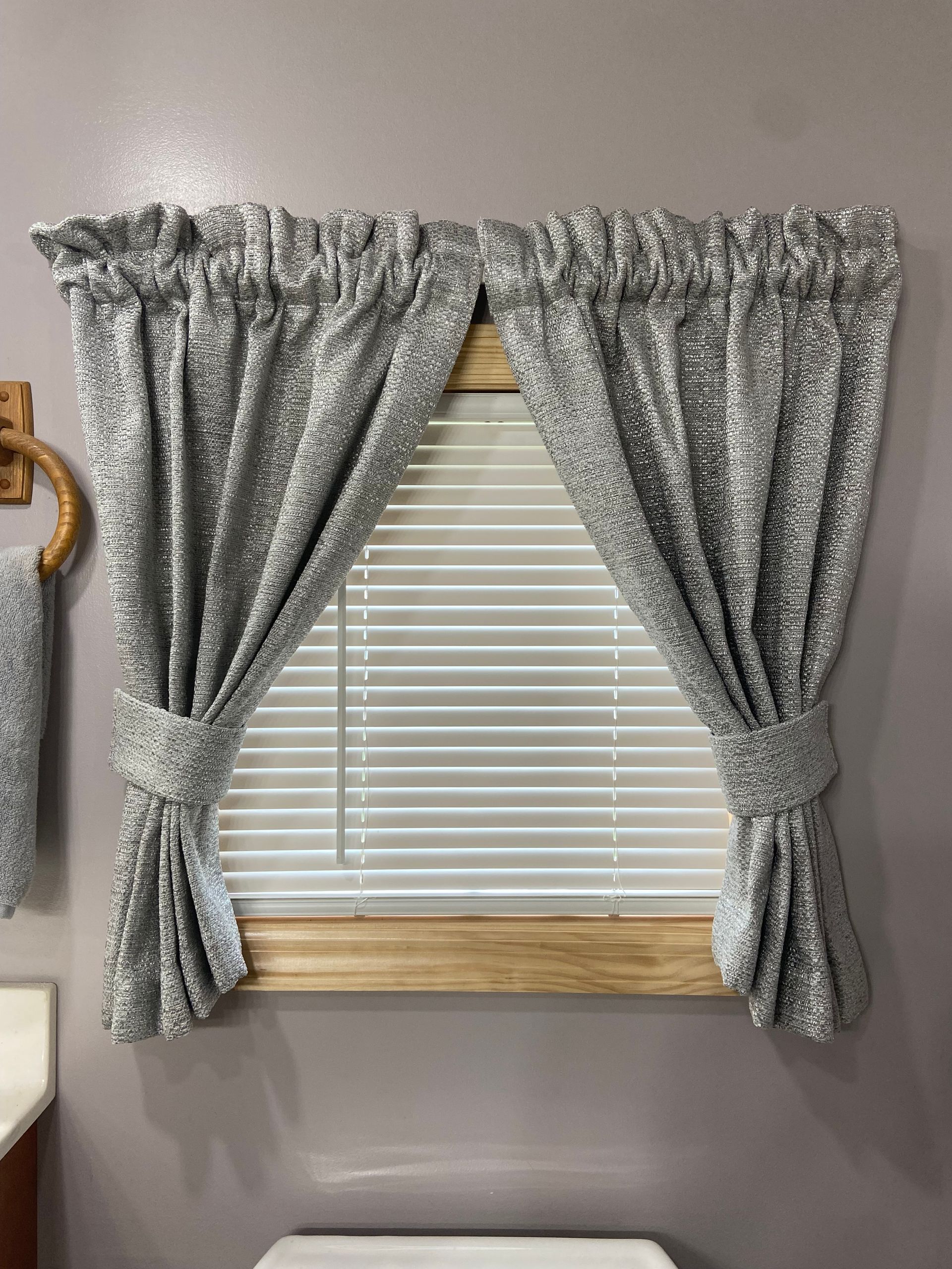 A window with blinds and curtains in a bathroom next to a toilet.