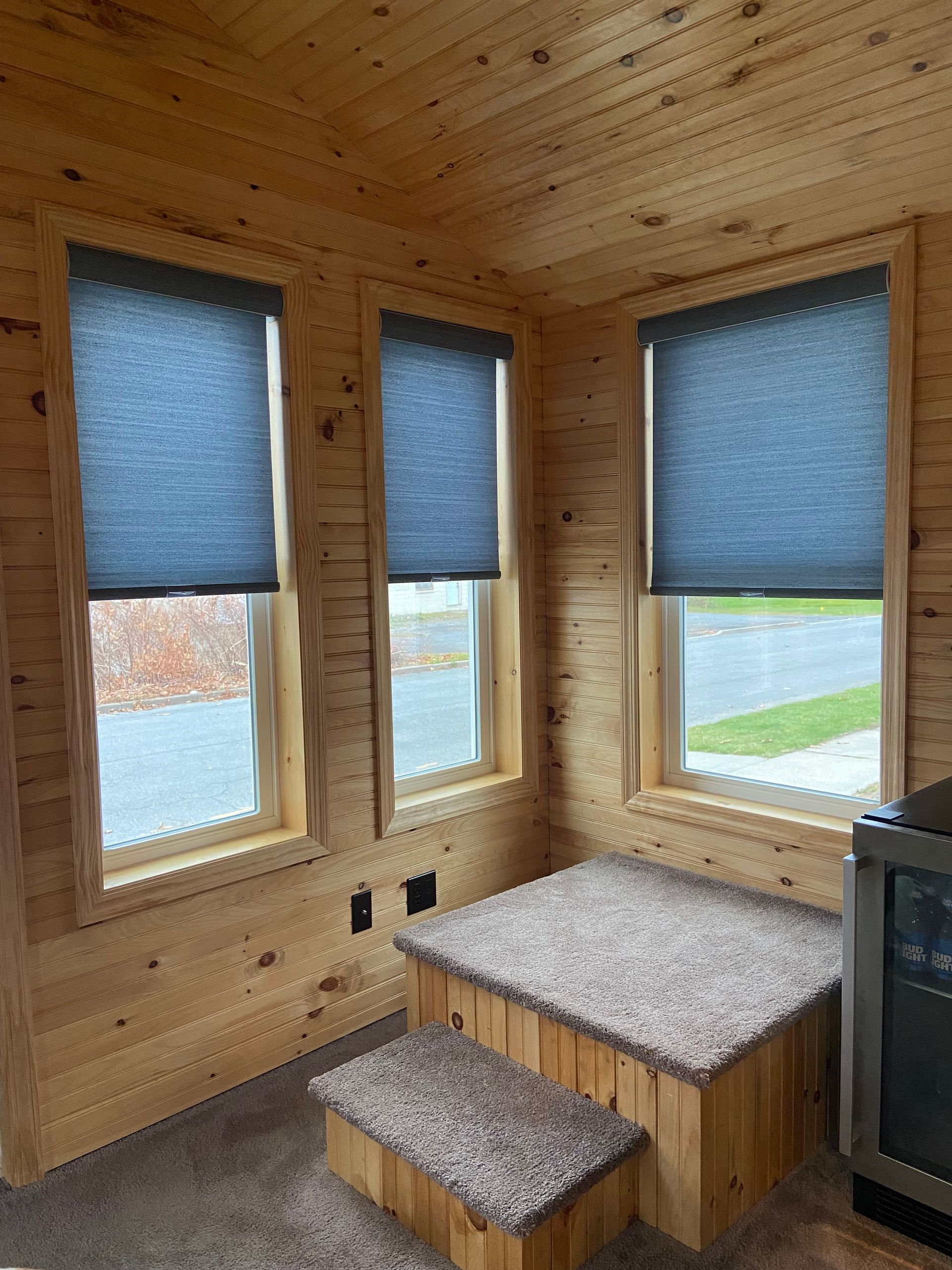 A room with wooden walls , blue blinds , and stairs.