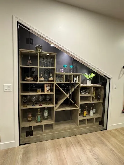 A wine rack is built under a staircase in a room.