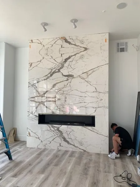 A man is kneeling in front of a marble fireplace in a living room.