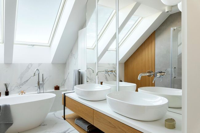 Modern bathroom with skylights, marble walls, wooden accents, and oval sinks.
