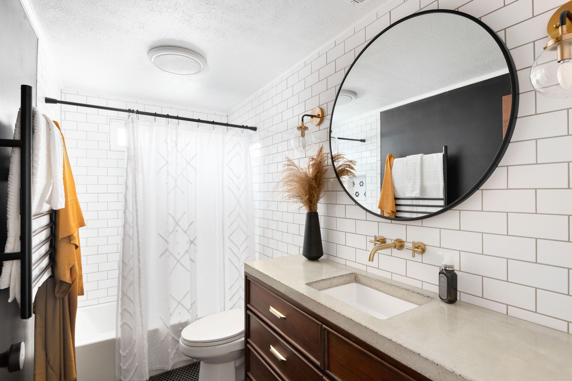 Modern bathroom with white subway tile, dark wood vanity, round mirror, and black accents.