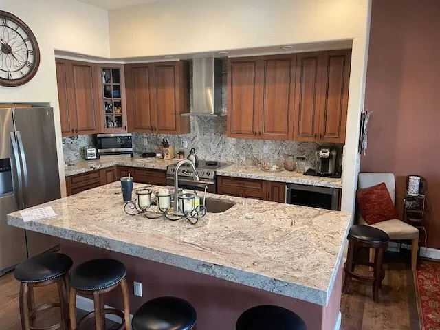 A kitchen with granite counter tops , stainless steel appliances , wooden cabinets and a clock on the wall.