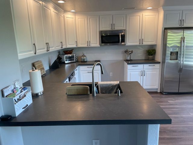 A kitchen with white cabinets , stainless steel appliances , a sink , and a refrigerator.