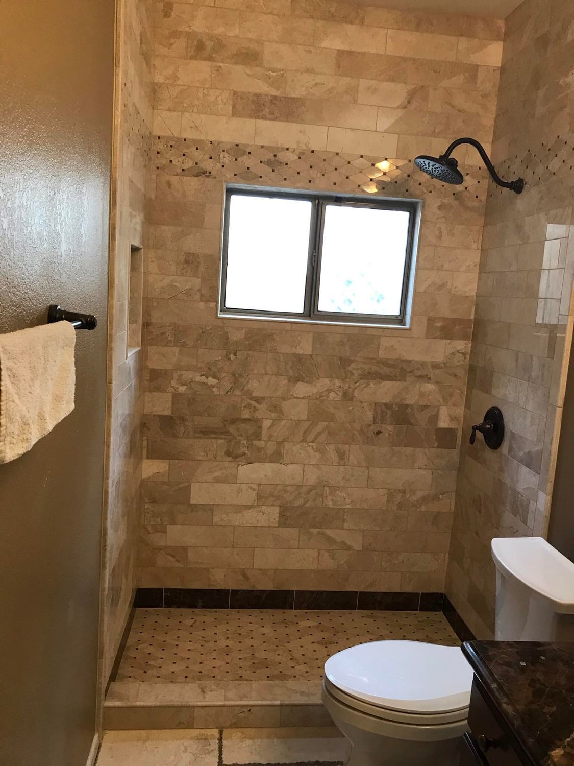 Shower with tiled walls, window, and a toilet. Beige tiles and dark fixtures.