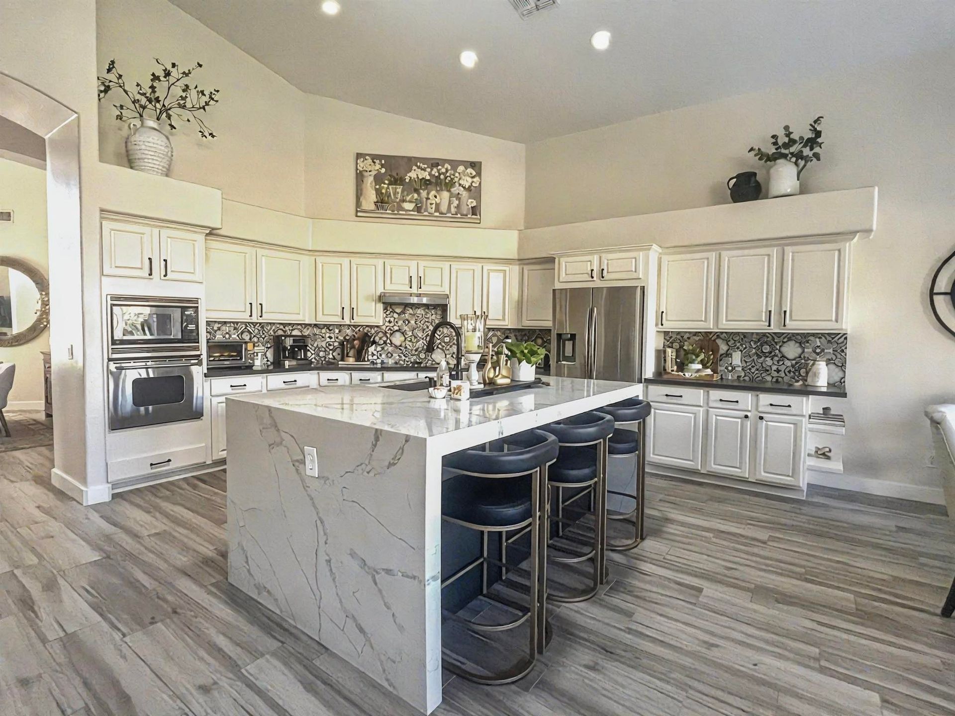 Modern kitchen with white cabinets, large island with seating, stainless steel appliances, and patterned backsplash.