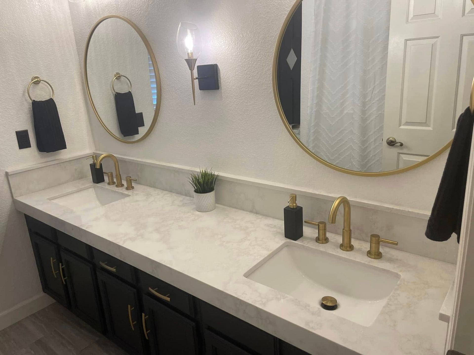 Bathroom with white countertop, black cabinets, gold fixtures, and round mirrors.