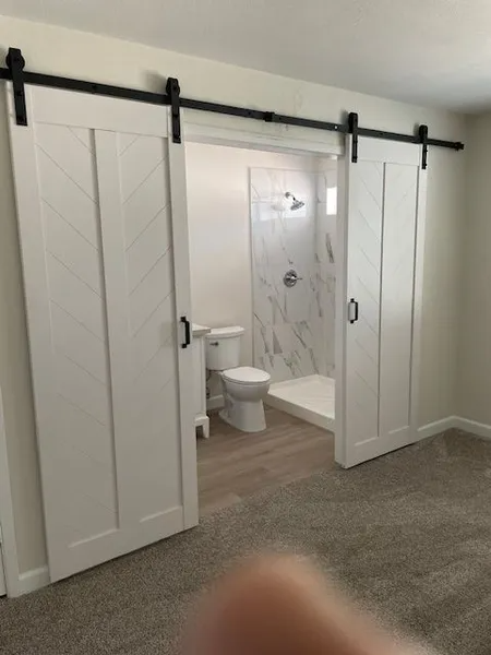 A bathroom with a toilet and shower behind sliding barn doors.