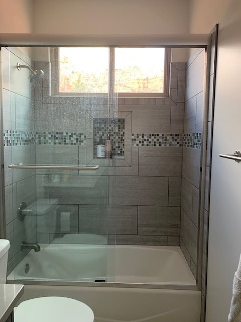 A bathroom with a tub , toilet , shower and window.