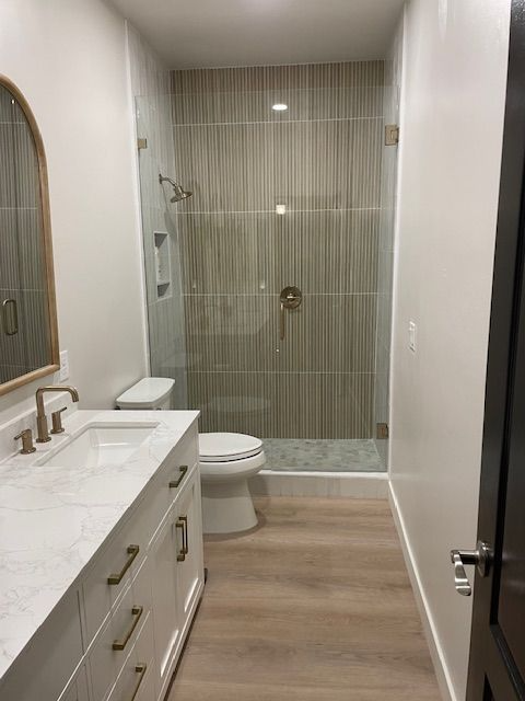 A bathroom with a toilet , sink , mirror and walk in shower.