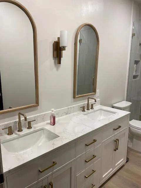 A bathroom with two sinks , two mirrors and a toilet.