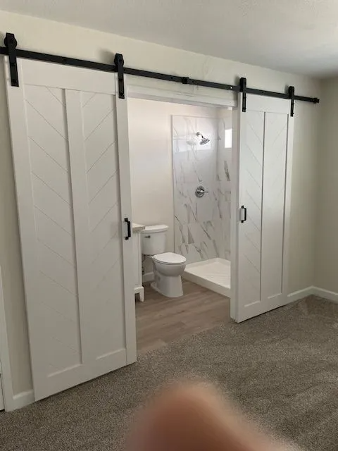 A bathroom with sliding barn doors leading to a toilet and shower.