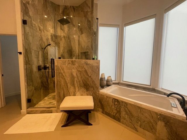 A bathroom with a tub , shower , and ottoman.