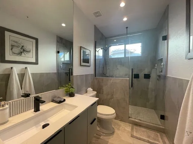 A bathroom with a toilet , sink , mirror and walk in shower.