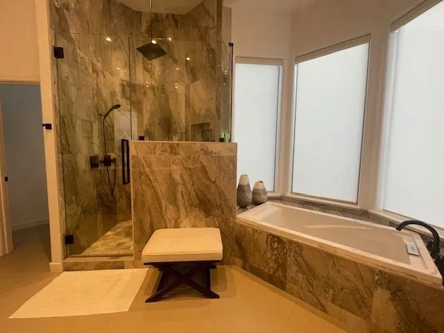 A bathroom with a tub , shower , and ottoman.