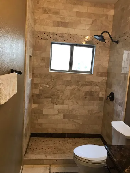 A bathroom with a toilet , shower , and window.