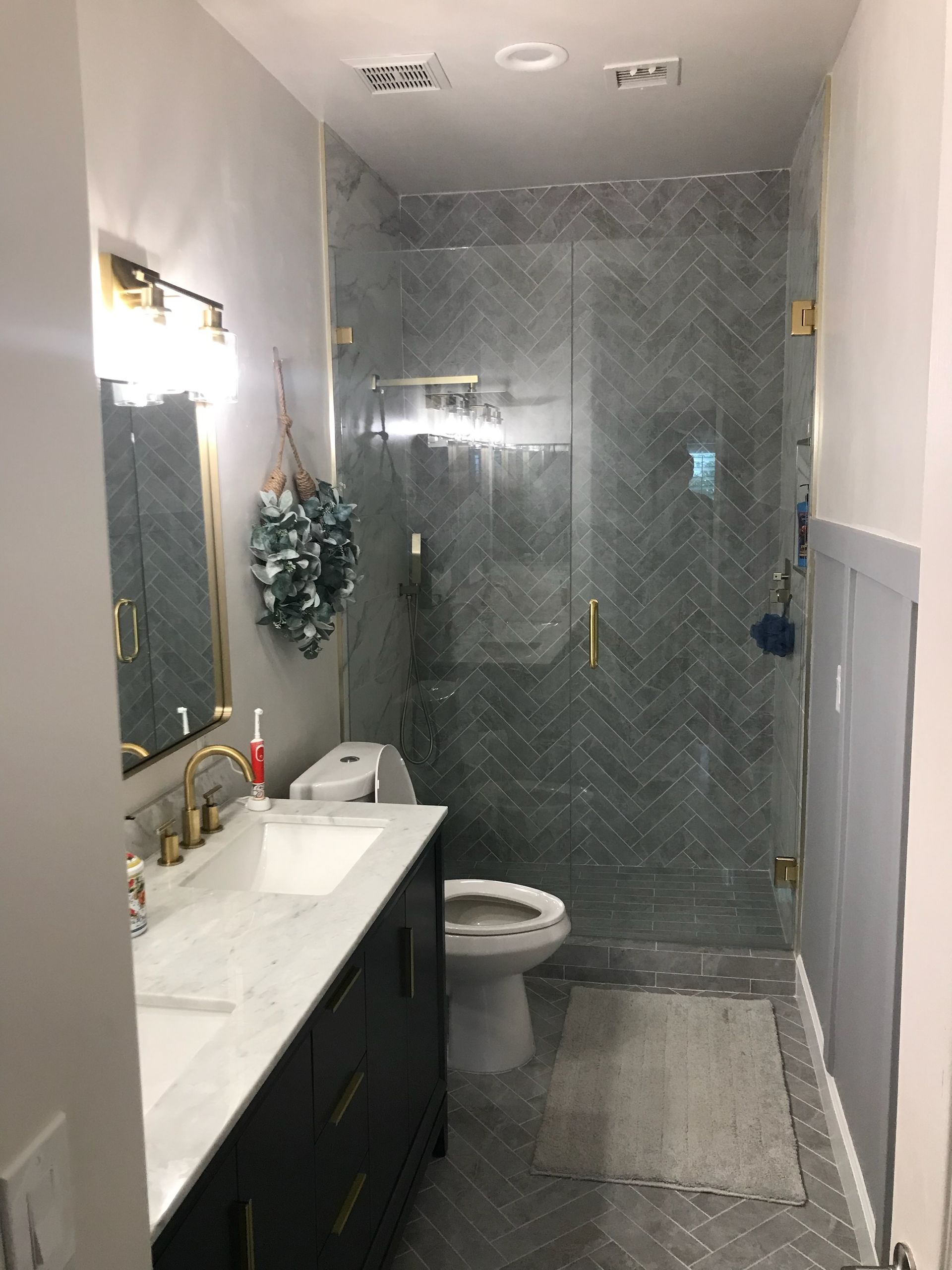 Bathroom with dark blue vanity, marble countertop, and gray herringbone tile shower.