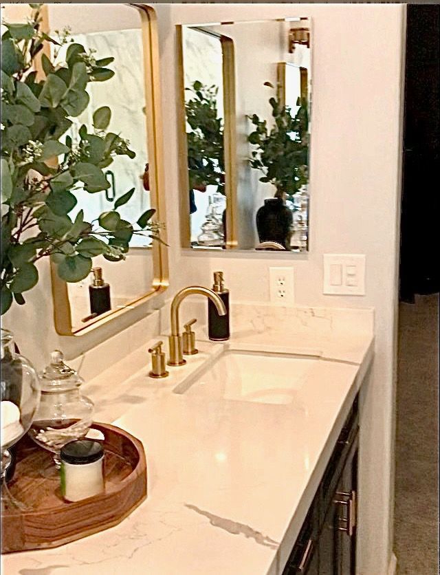 Bathroom vanity with gold fixtures, marble countertop, and eucalyptus greenery.