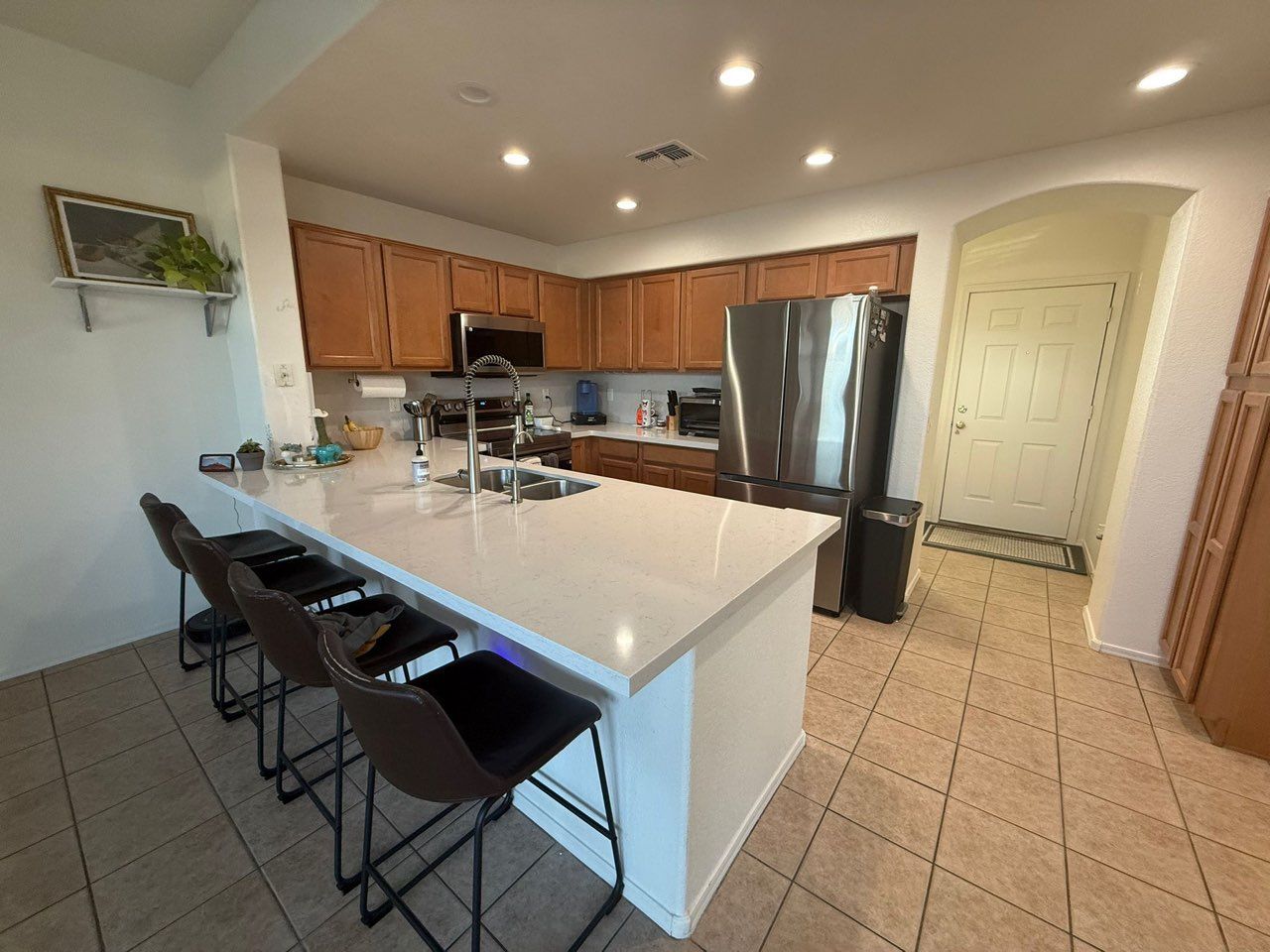 A kitchen with a large island , stools and a refrigerator.