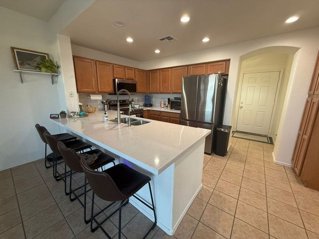 Kitchen with brown cabinets, white countertop island, stainless steel appliances, bar stools, and arched doorway.