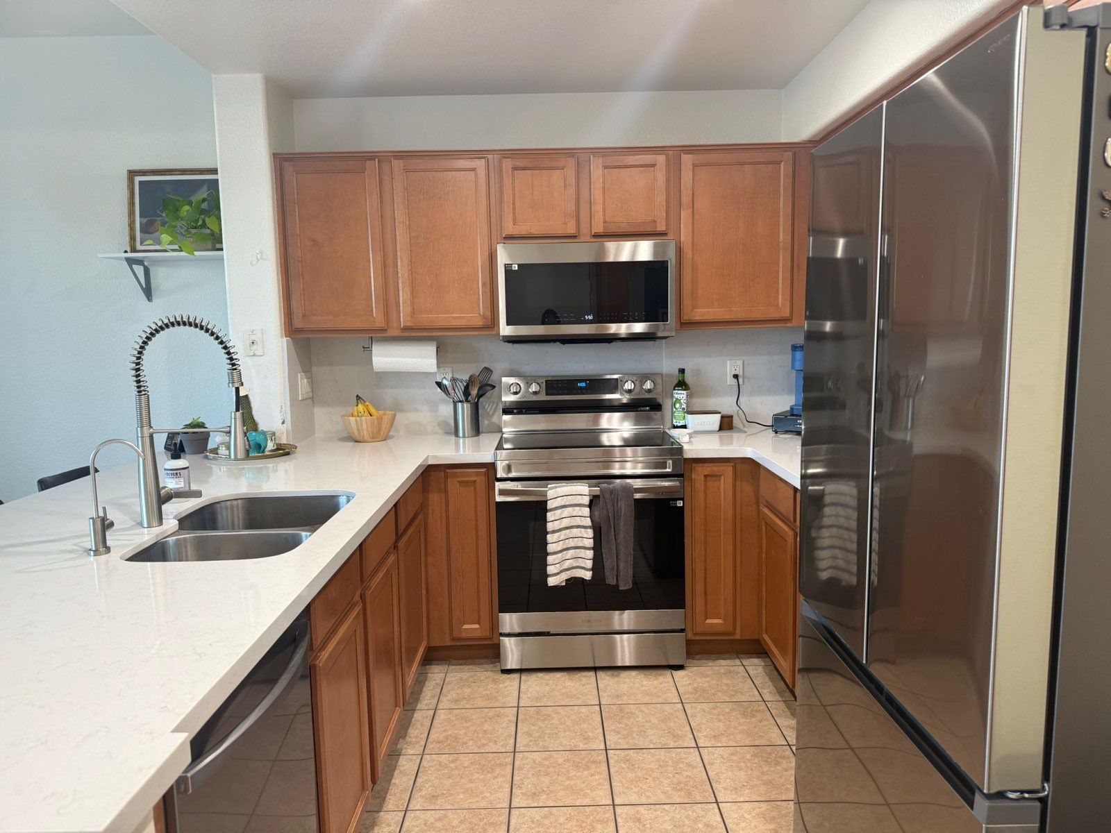 U-shaped kitchen with light countertops, wood cabinets, stainless steel appliances, and tile floor.