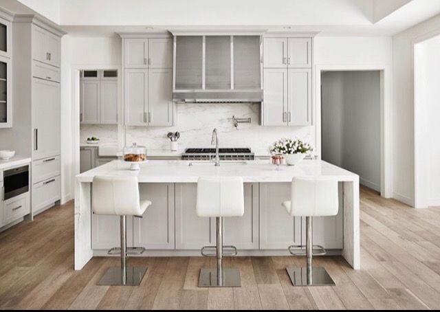 Modern, light gray kitchen with white island, bar stools, and wood flooring.
