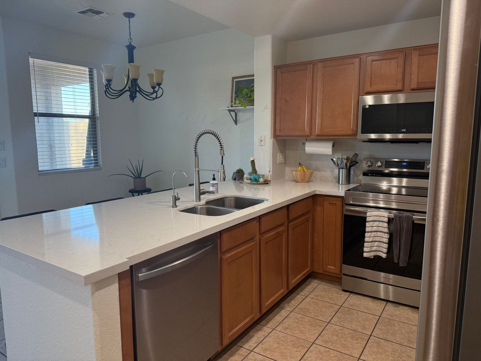 Kitchen with light countertops, wooden cabinets, stainless steel appliances, and a window.