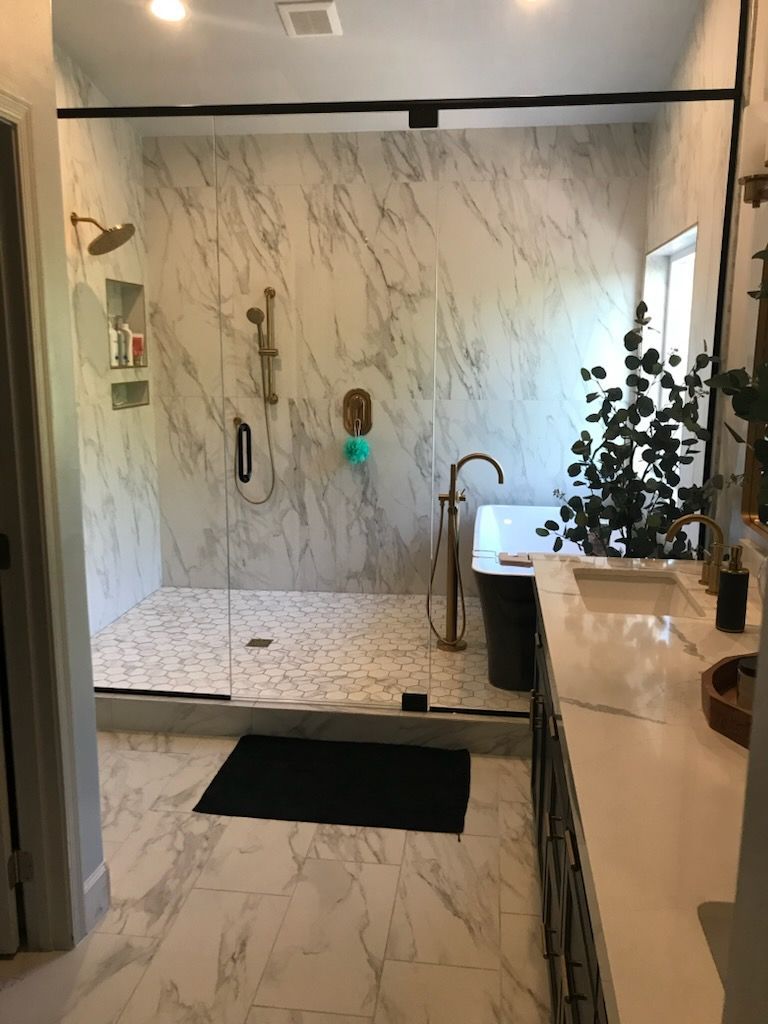 Luxurious bathroom with marble tiles, glass shower, gold fixtures, and a freestanding bathtub.