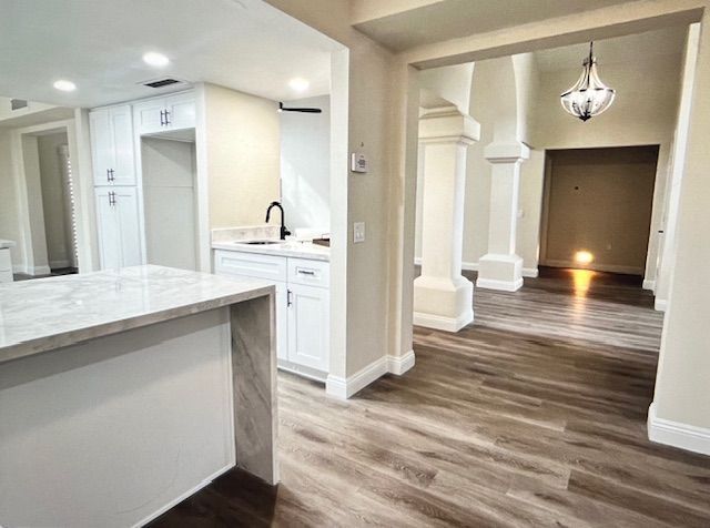 A kitchen with white cabinets and hardwood floors and a chandelier hanging from the ceiling.