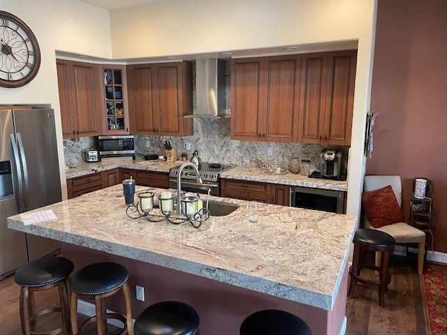 A kitchen with granite counter tops , stainless steel appliances , wooden cabinets and a clock on the wall.