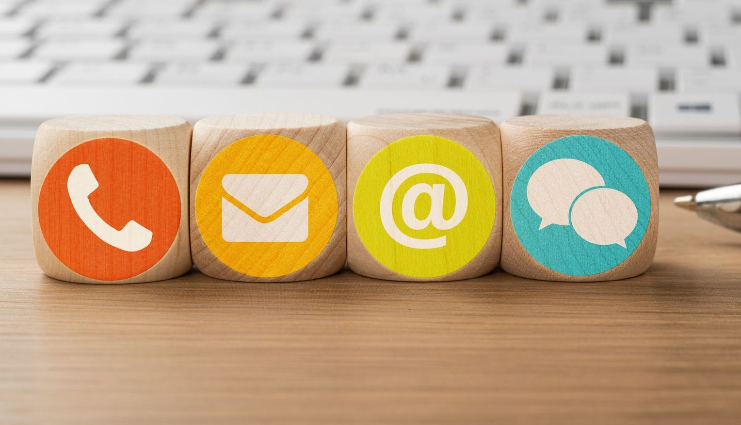 Quattro cubi di legno con delle icone sopra sono appoggiati su un tavolo di legno davanti a una tastiera.