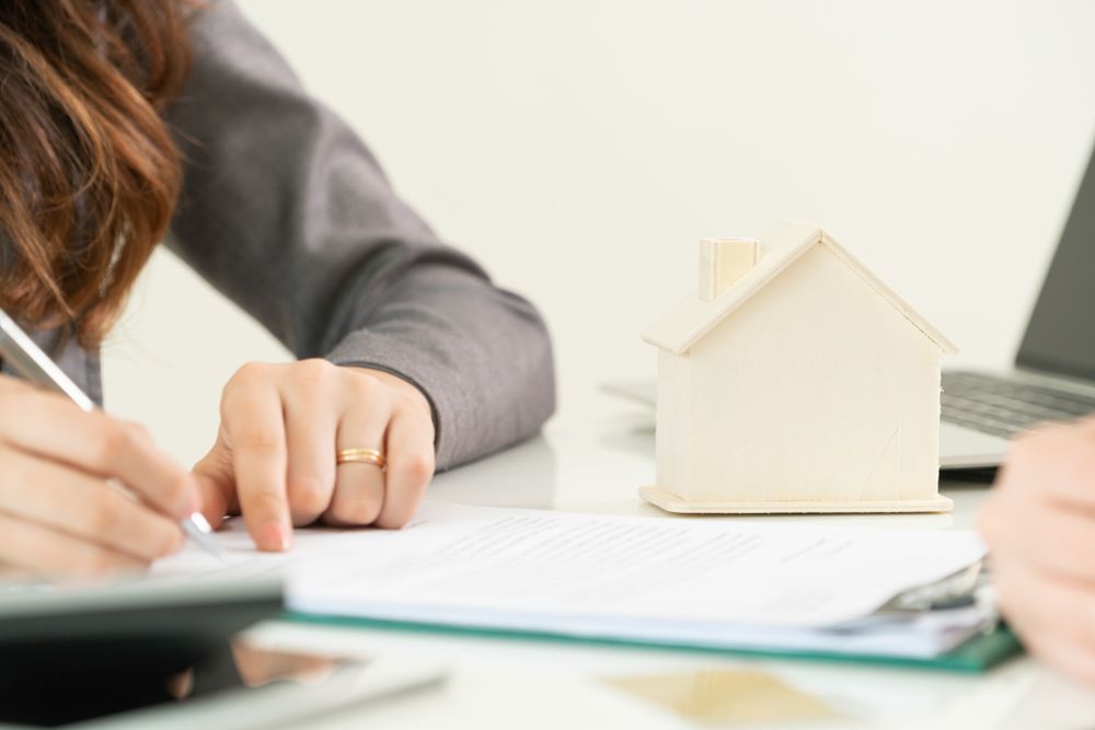 Person Signing Document With Wooden House Model and Laptop on Desk — Adamson Town Planning in Noosaville, QLD